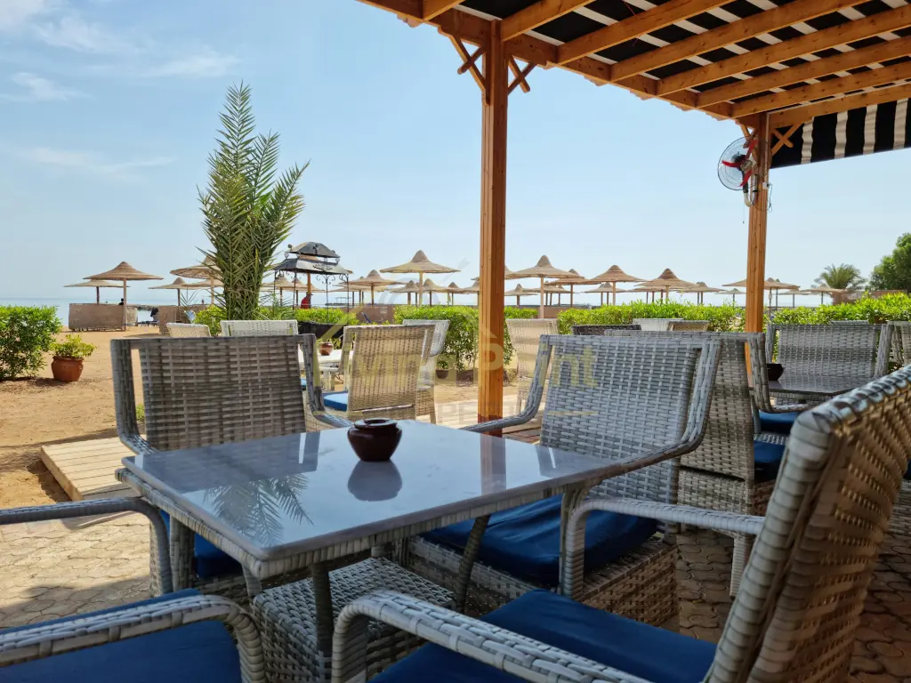 Korbsitzgruppe unter einer Holzpergola neben dem Strand